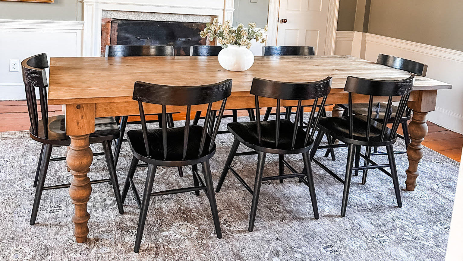 An eight-foot pine farmhouse table surrounded by black dining chairs